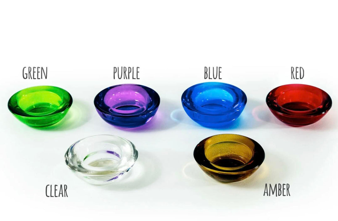 A collection of votive glasses in various colors including green, purple, blue, red, and clear, each designed to hold a standard tealight candle.