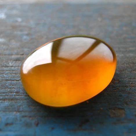 A close-up image of a piece of amber with a reflective surface on a wooden surface.
