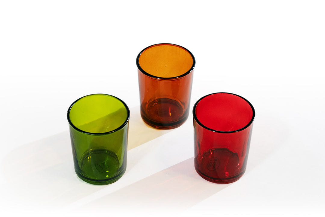 Three votive glasses in green, amber, and red colors, displayed on a white background.