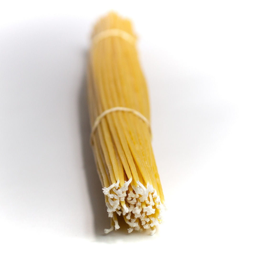 A bundle of beeswax tapers with visible wicks and a light coating of wax on the surface, tied with a string.