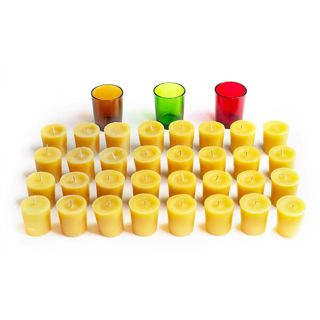 An array of yellow votive candles arranged in rows with a selection of votive glasses in amber, green, and red colors displayed in the background.