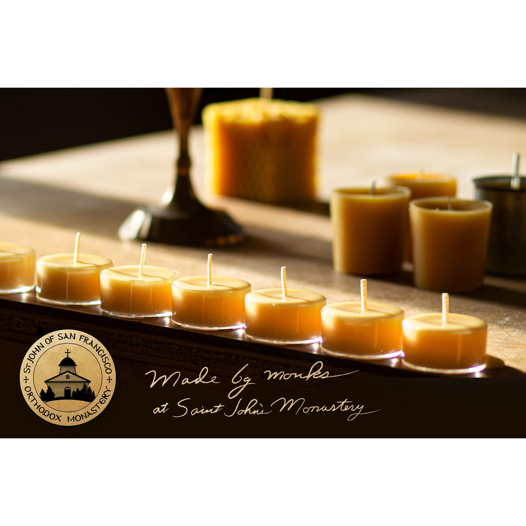 A group of yellow beeswax tealight candles arranged on a wooden surface, with the monastery's seal and signature indicating they are handcrafted at Saint John Monastery.