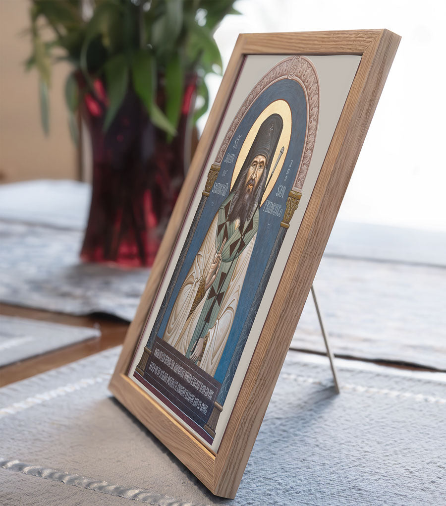 Framed religious icon on a textured surface with a blurred plant in the background.
