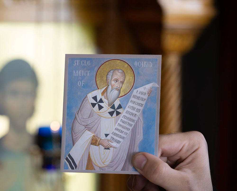 Hand holding a card with a religious Icon of St Clement in a blurred indoor setting