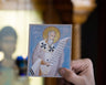 Hand holding a card with a religious Icon of St Clement in a blurred indoor setting