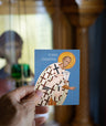 Hand holding a card with an illustration of St. John Chrysostom against a blurred indoor background.