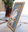 Framed religious icon of St. John Chrysostom on a blue background, placed on a textured surface.