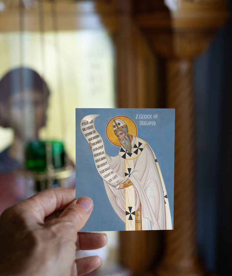 Hand holding a card with an illustration of a Saint Patrick against a blurred indoor background