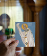 Hand holding a card with an illustration of a Saint Patrick against a blurred indoor background