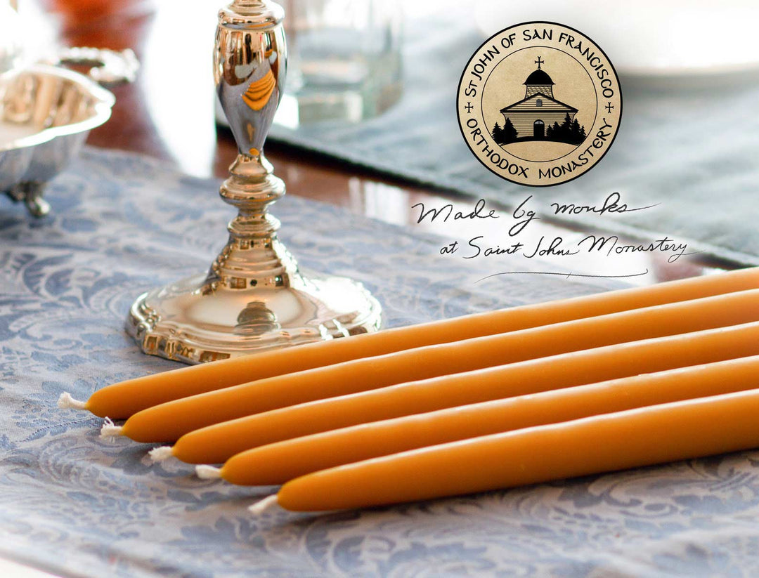 5 100% Pure Beeswax Dinner Candles and candle holder, on a blue table cloth with st. john's monastery logo