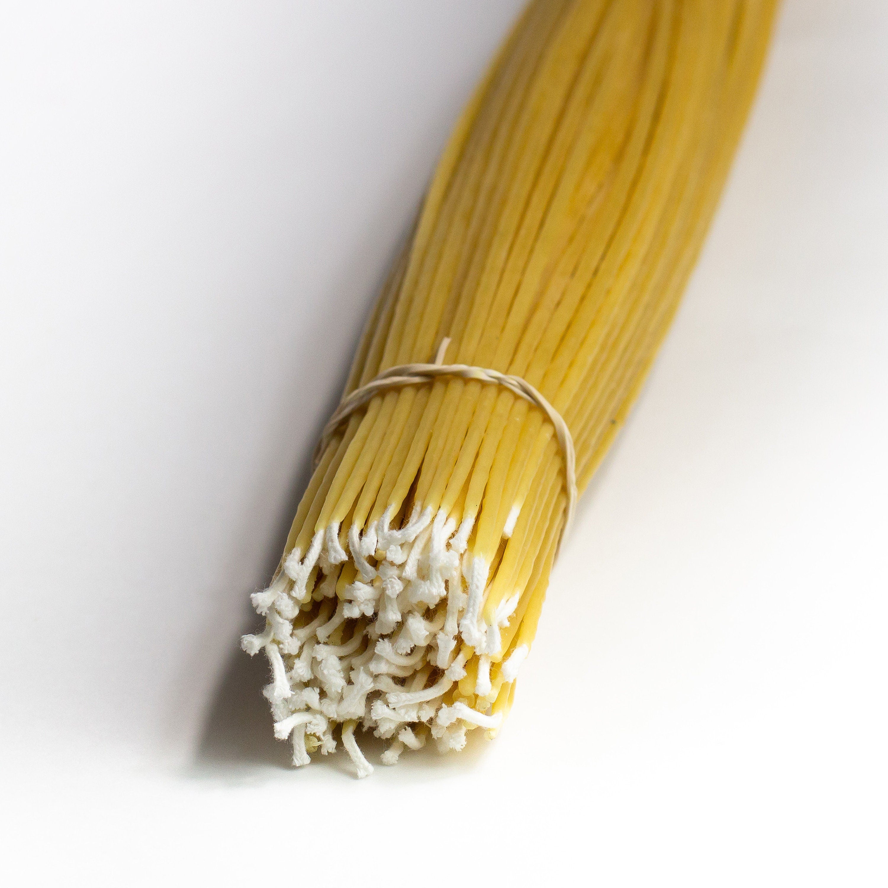 A bundle of light beige colored wax taper candles bound together, with an elastic band.